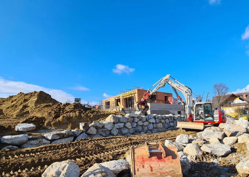 Steinmauerbau mit Bagger auf Baustelle eines Einfamilienhauses – Bauunternehmen Pierer bei Erd- und Hochbauarbeiten in der Steiermark